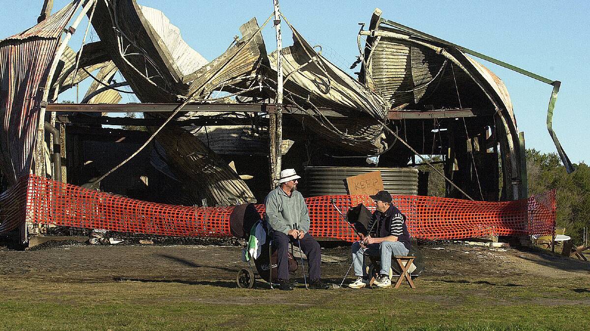 11/08/2003 GUTTED: Golfers Richard Davey and Terry Mickleborough contemplate their game and the future of the club, sitting in front of the burnt out Freycinet Golf Club house.