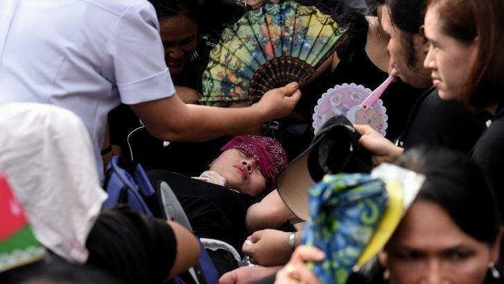 A woman faints outside the Grand Palace in Bangkok waiting for the body of the king. Photo: Kate Geraghty