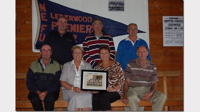 Descendants of Legerwood's 1952 premiership-winning football team with the flag and a photo of the winning team. Graeme Walsh, Kevin Coates, Danny Nichols, Brian Walsh, Jill Flowers, Marlene Russell, and Mike Walsh.