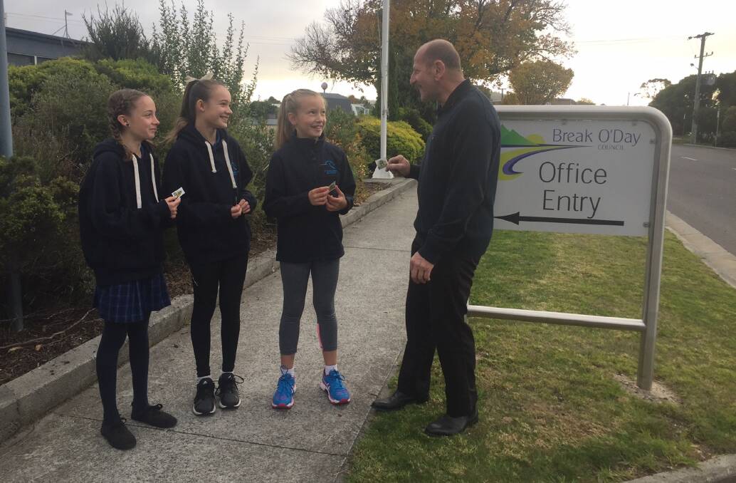 POUNDING THE PAVEMENT: Miette and Amelie Richardson and Sophie Lowry take a sticker from Break O'Day mayor Mick Tucker on Walk Safely to School Day. Picture: supplied.
