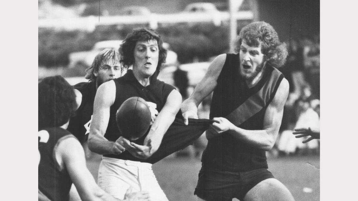 Launceston half-back Gary Davis gets himself out of trouble with a quick handball as North player Graeme Hunnibell grabs him by the guernsey. 1974.