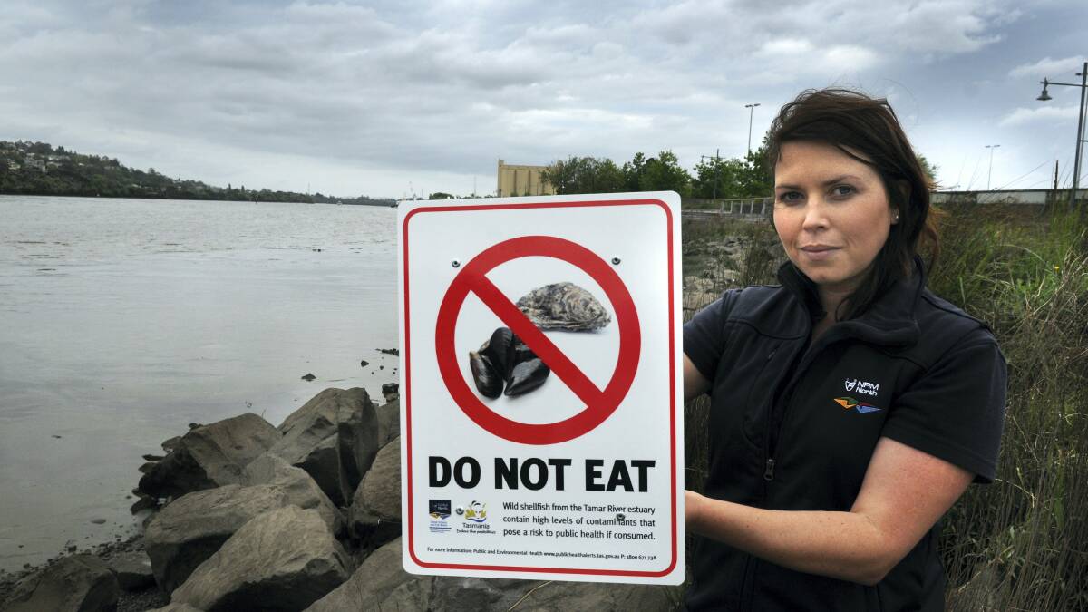 TEER project officer Monique  Thompson alongside a sign warning not to eat oysters from the Tamar.  