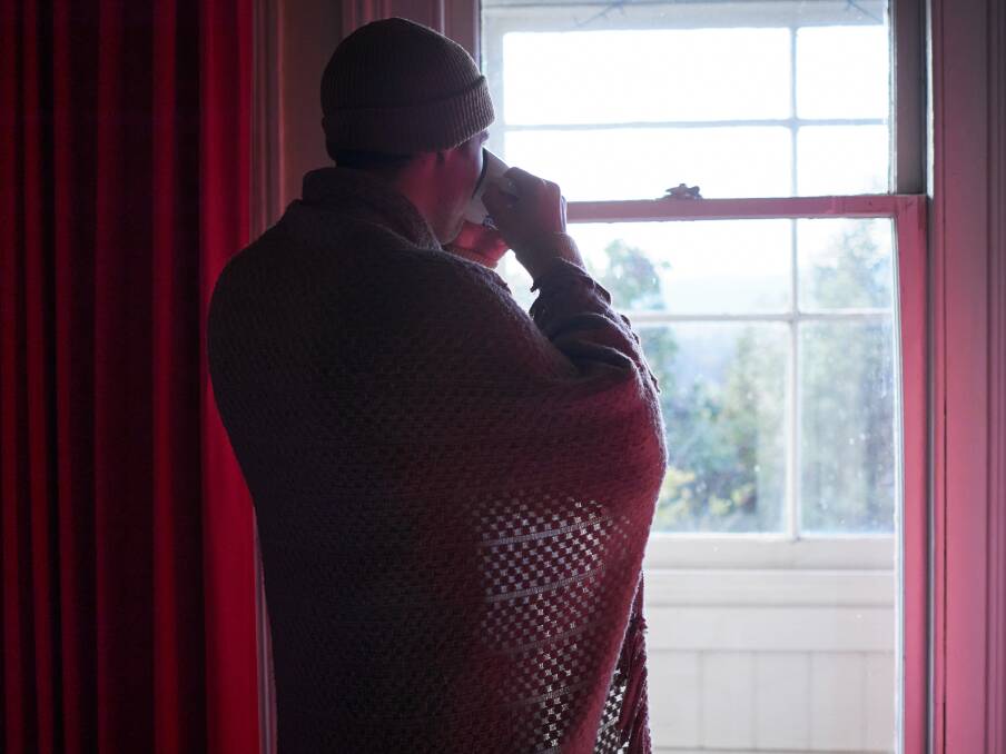 A man in a beanie and blanket standing near a window. Picture by Rod Thompson. 