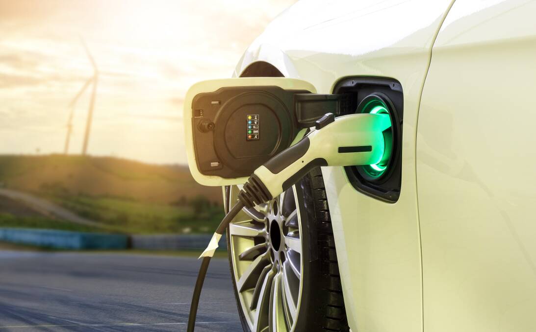 Electric car or EV car charging in station on blurred of sunset with wind turbines in front of car on background. Picture from Shutterstock. 