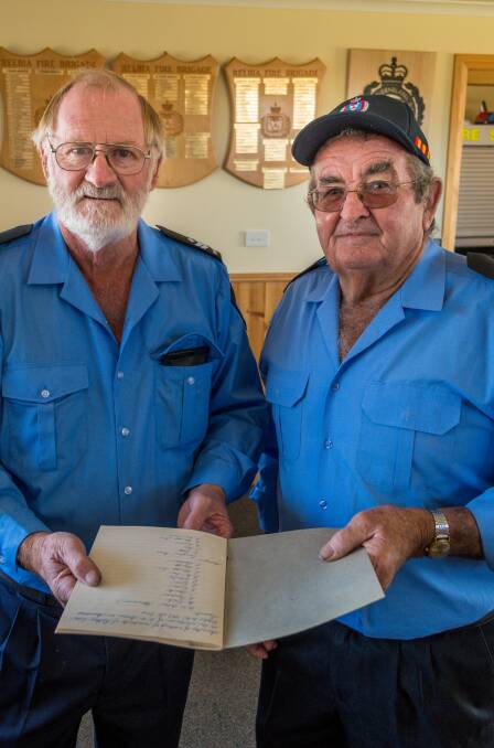 Volunteer firefighters Rodney Springer and Greg Wise with a book of minutes dating back to the first meeting. 