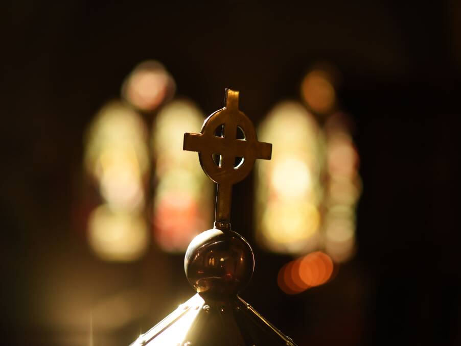 SMALL DETAILS: A cross, with the shimmer of stained-glass windows in the background. 