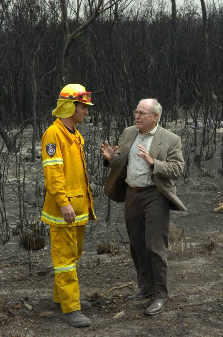 Former Prime Minister John Howard flew in to Tasmania's fire ravaged East Coast to express the country's profound admiration for the State's firefighters, pictured here with Launceston Fire station officer Heath Bracey in burnt out scrub near Scamander.