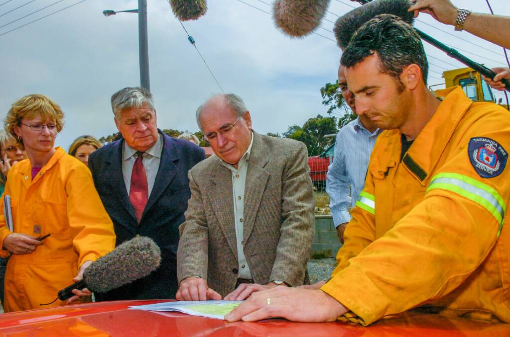 Former Prime Minister John Howard is accompanied by former Break O'Day Mayor the late Robert Legge are shown a map of the area by Launceston Fire station officer Heath Bracey while on the fire scene at Scamander.