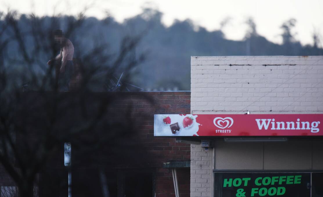 NEGOTIATIONS: A man on the roof of the property adjoing the Winning Post Takeaway speaks to police on the ground. Picture: Scott Gelston.