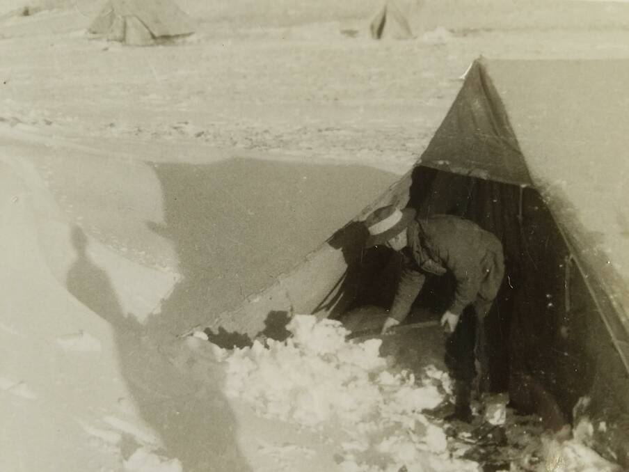 A man shoveling snow from around a desert tent during his deployment.