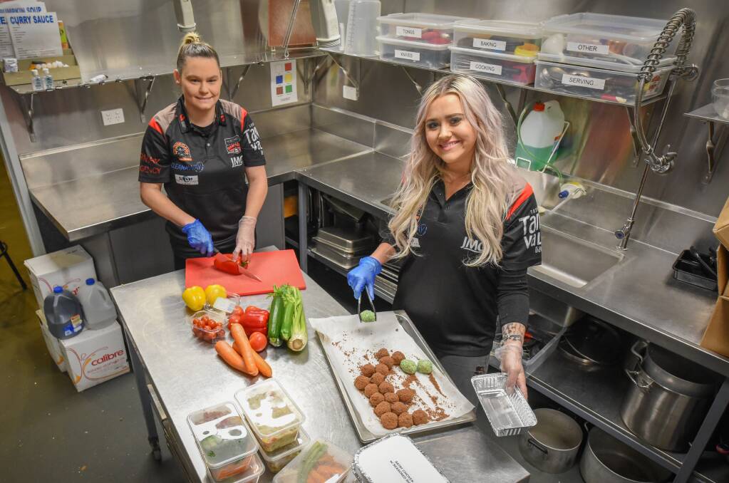 EAT OUT: North Launceston Football Club kitchen manager Jarrah Nixon and Bombers volunteer Kelsey Sheriff prepare ingredients in packed meals to go out to the community amid the ongoing COVID-19 pandemic. Picture: Paul Scambler