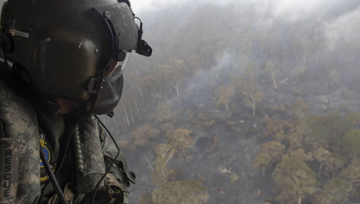 A member of the defence force in a maritime support helicopter above burnt land in southern NSW. Picture: Department of Defence