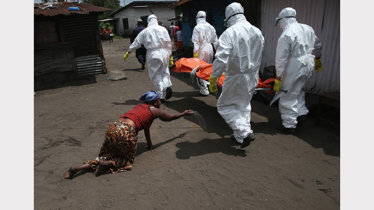 A woman throws soil towards the body of her sister who died of Ebola – burial team
members bear the body away for cremation. Picture: Getty Images